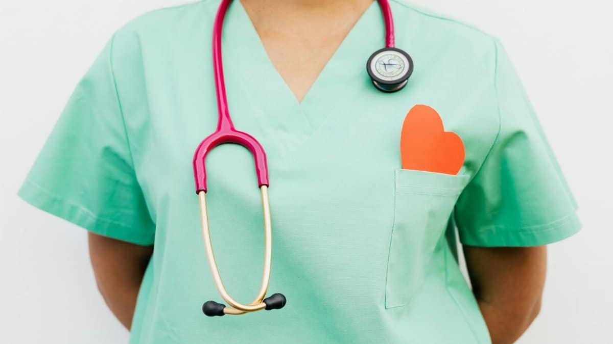 Close-up of a medical professional with a stethoscope and a paper heart cutout on a green uniform pocket.