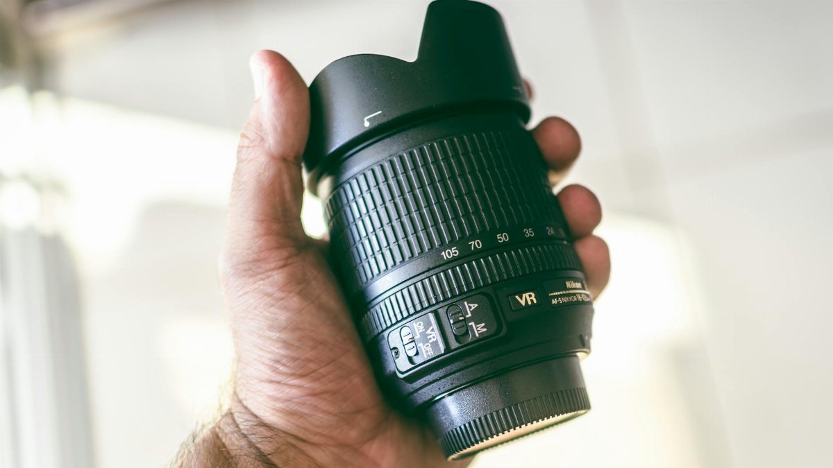 A person holding a camera lens in a well-lit indoor setting, showcasing lens details.