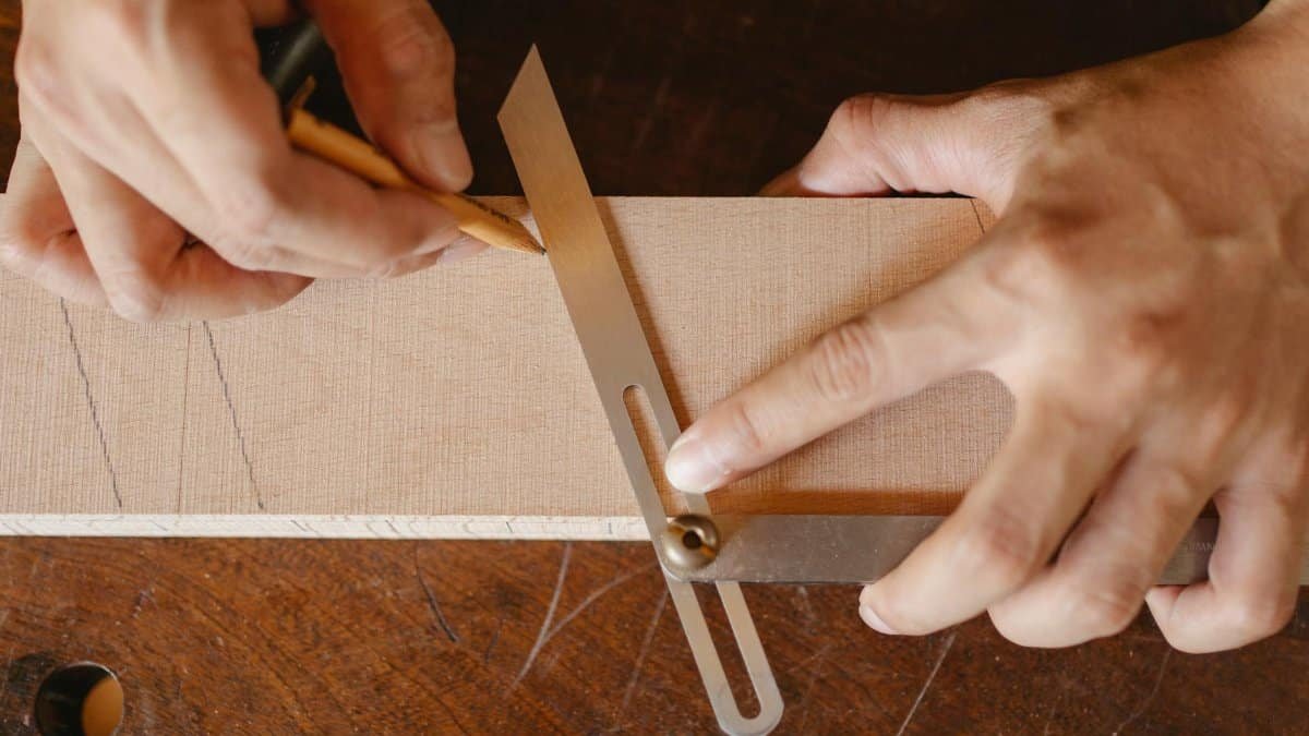 Top view of crop anonymous woodworker drawing diagonal line on wooden block using bevel on workbench