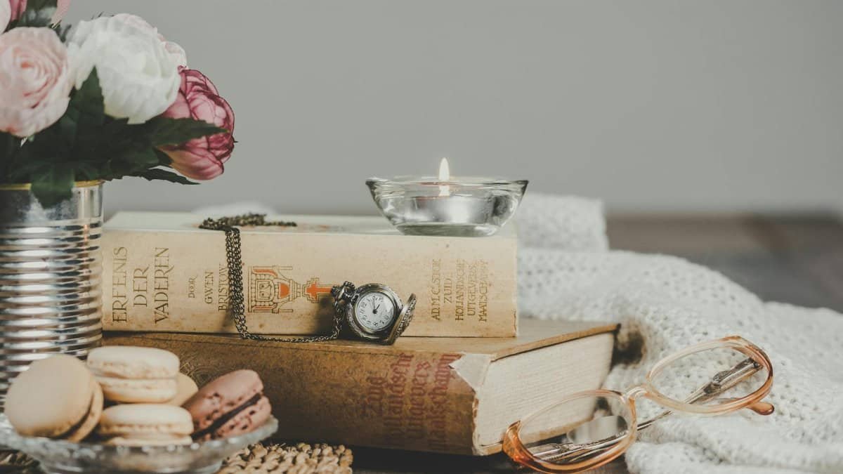 Vintage still life with books, macarons, candle, and flowers on a cozy table.