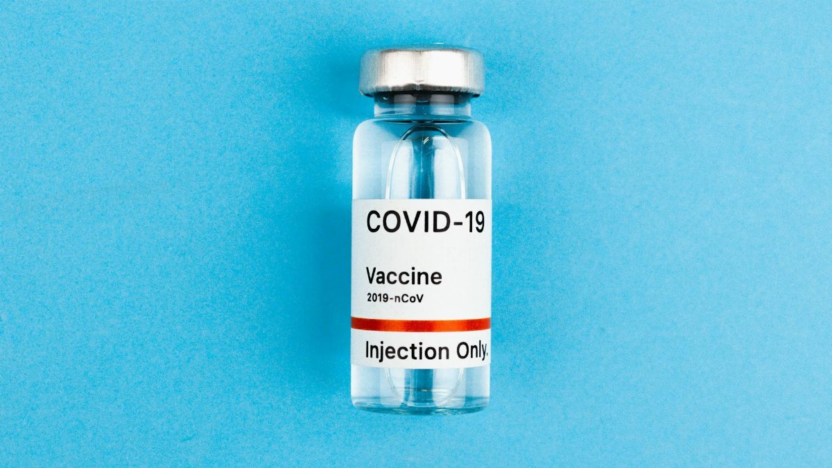 Glass vial labeled COVID-19 vaccine placed on a light blue surface, symbolizing medical advances.