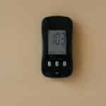 Close-up of a blood glucose meter displaying 103 mg/dL on beige surface.