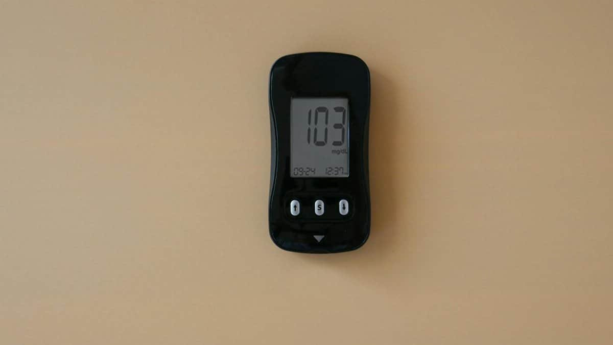 Close-up of a blood glucose meter displaying 103 mg/dL on beige surface.