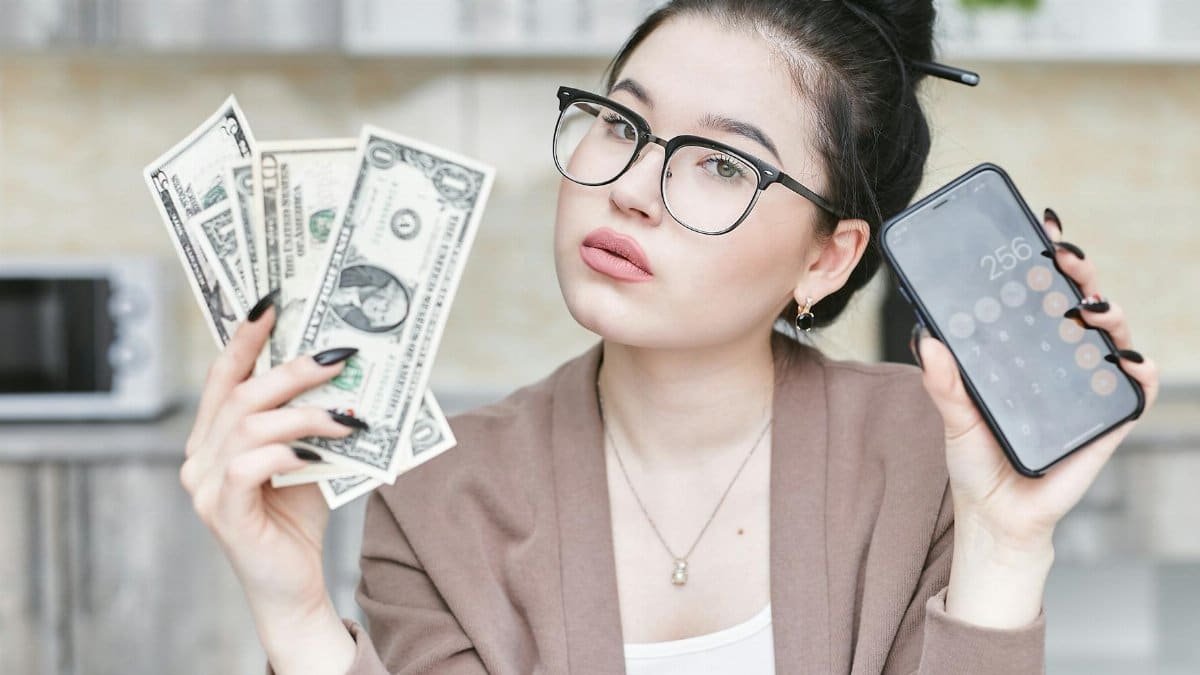 Woman holding cash and smartphone displaying calculator, highlighting personal finance management.