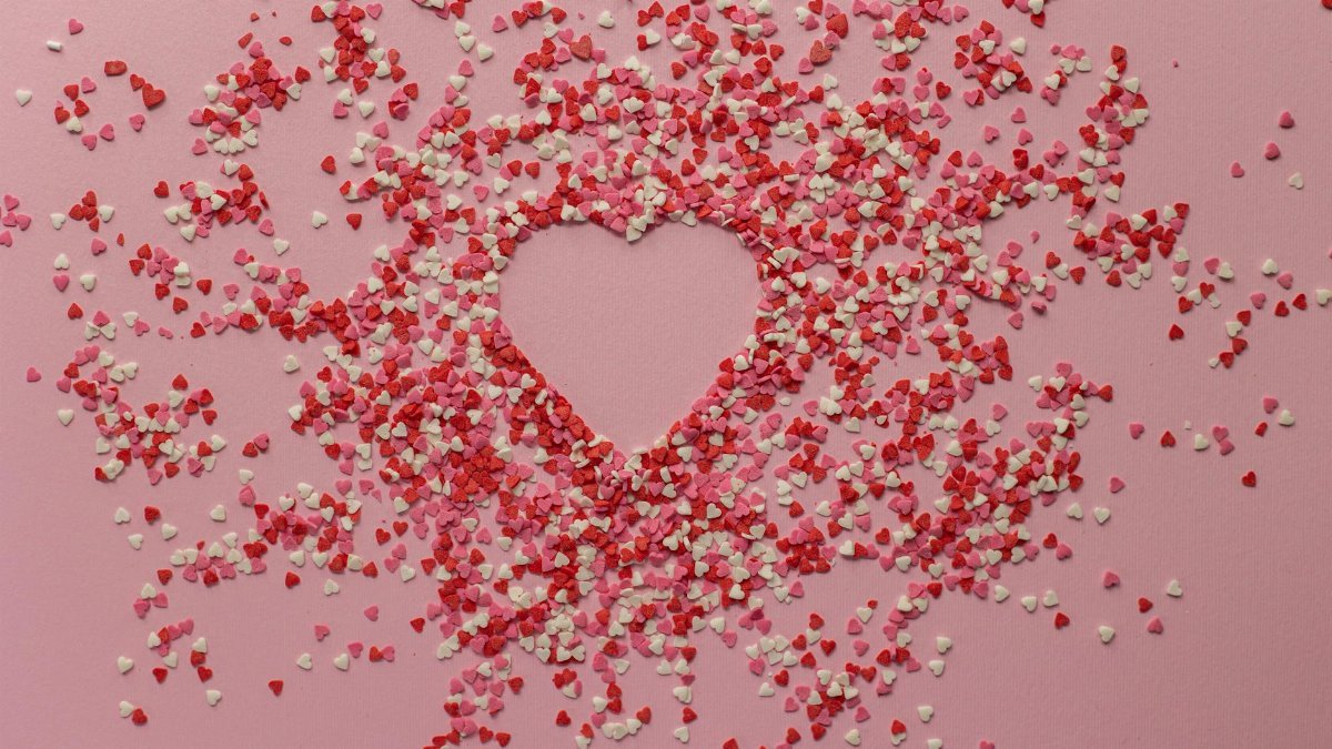 Heart-shaped red and white confetti scattered over a pink surface, perfect for Valentine's Day.