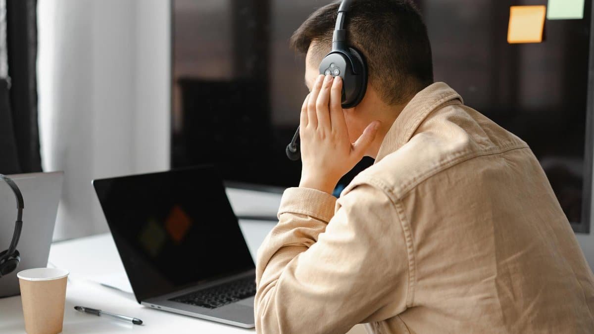 A man wearing headphones works at a laptop in a modern office setting.