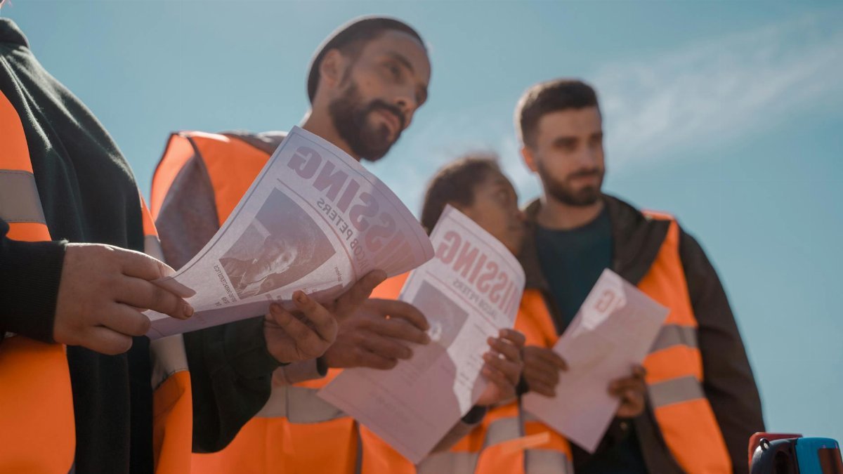 Group of volunteers in orange vests distributing missing person flyers outdoors.