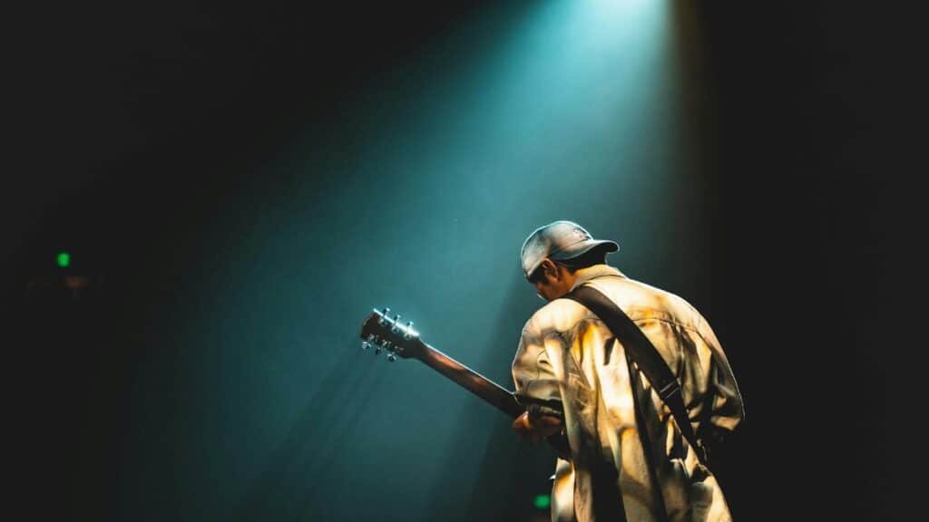 A musician performing live on stage under dramatic lighting, playing a guitar.