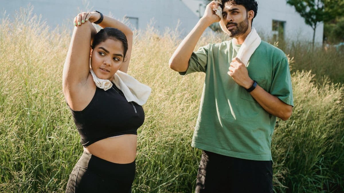 Pair stretching outdoors with towels around necks; fitness and health focus.