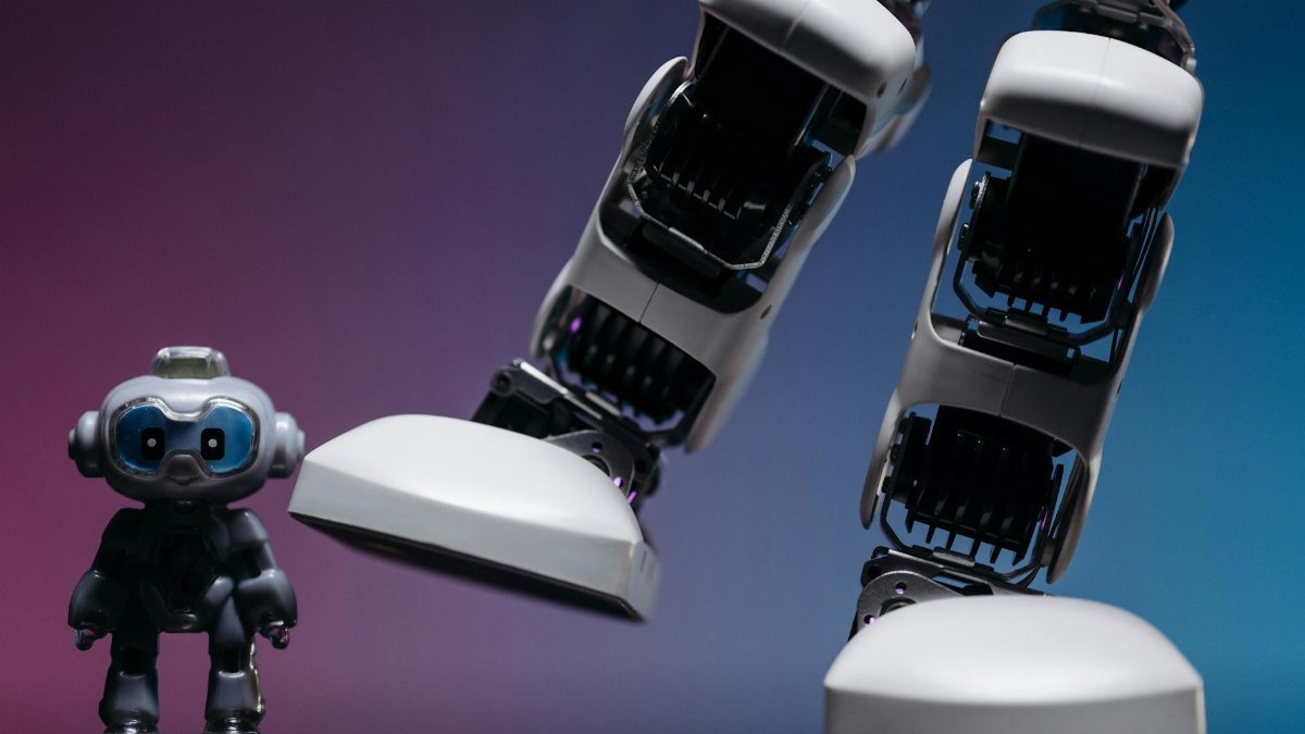 Close-up of small robot toy and large robotic leg in a moody studio setting.