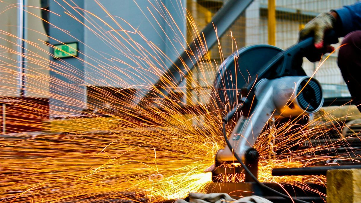A worker operates a grinder cutting metal, creating a vibrant display of sparks in an industrial setting.