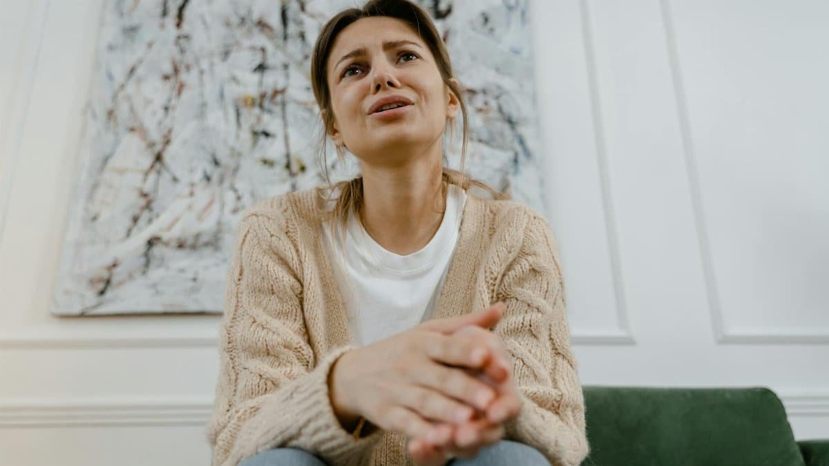 A woman in a cozy sweater is sitting indoors, expressing distress and frustration.