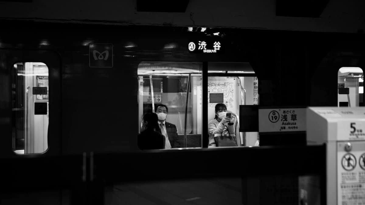 Black and white photo of people seated in Shibuya subway, Tokyo, with urban night ambiance.