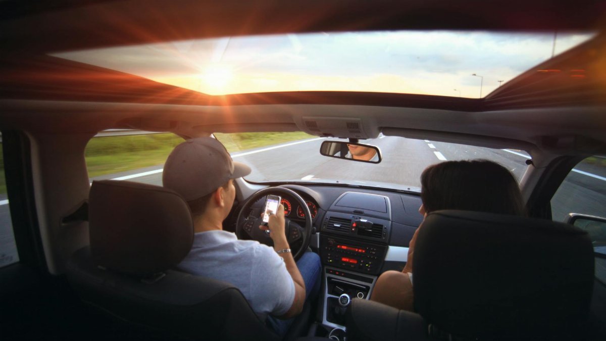 Driver using phone while driving at sunset with passenger in vehicle.