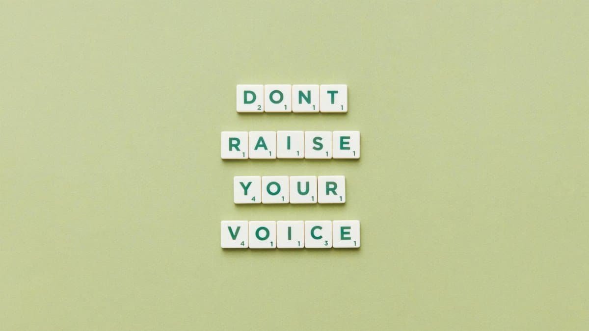 Scrabble tiles spelling 'Don't Raise Your Voice' on a green background.