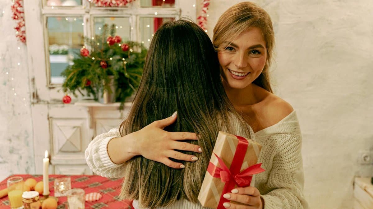 Happy woman giving a wrapped gift during a cozy Christmas celebration indoors.