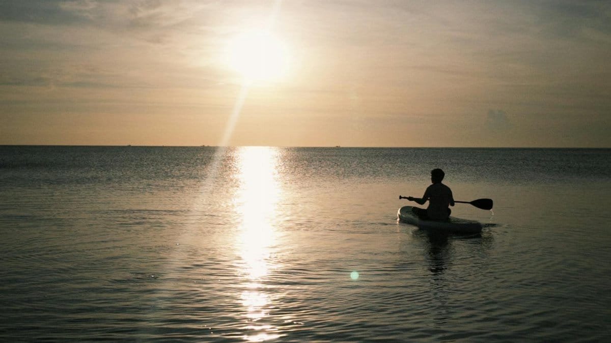 A person kayaking on calm ocean waters during a beautiful sunrise, exuding peace and solitude.