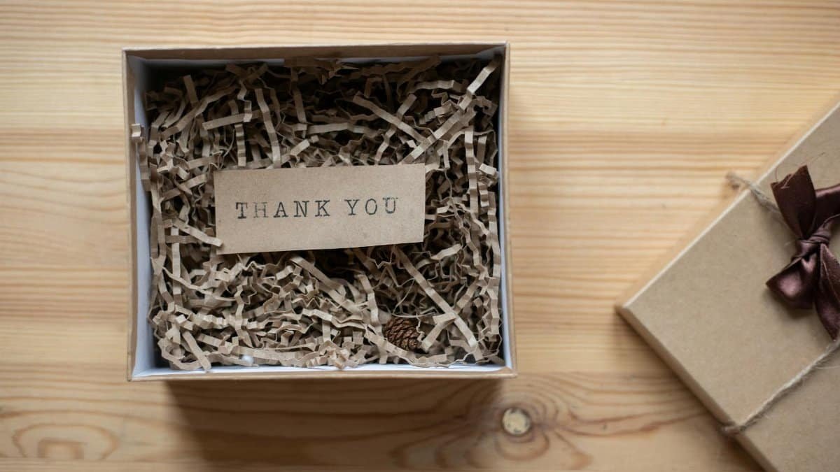 Top view of opened carton present box with small postcard with Thank You inscription and paper stuffing on wooden table