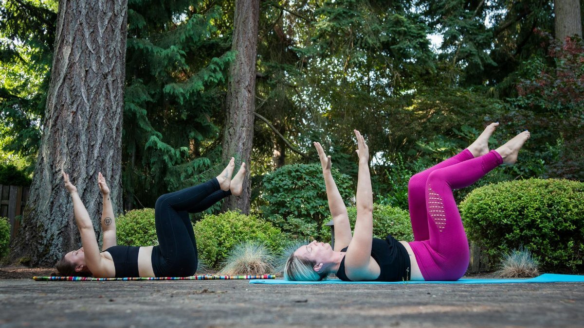 Two women practicing yoga outdoors, focusing on fitness and relaxation in a serene forest setting.