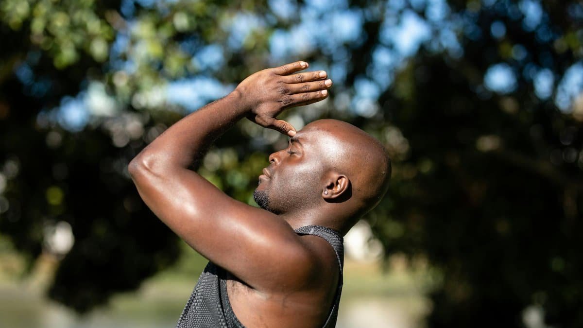 A bald man meditating and practicing yoga outdoors with a blurred natural background.