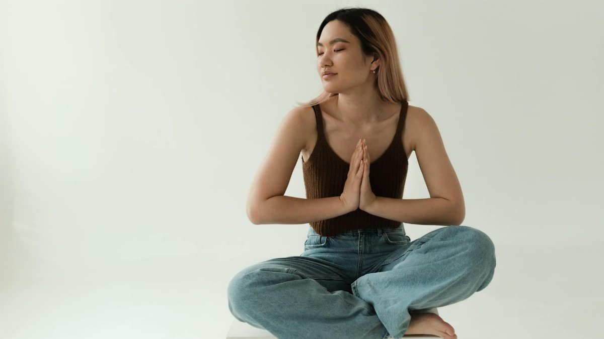 A serene adult woman in a yoga pose, meditating indoors with eyes closed in a peaceful setting.