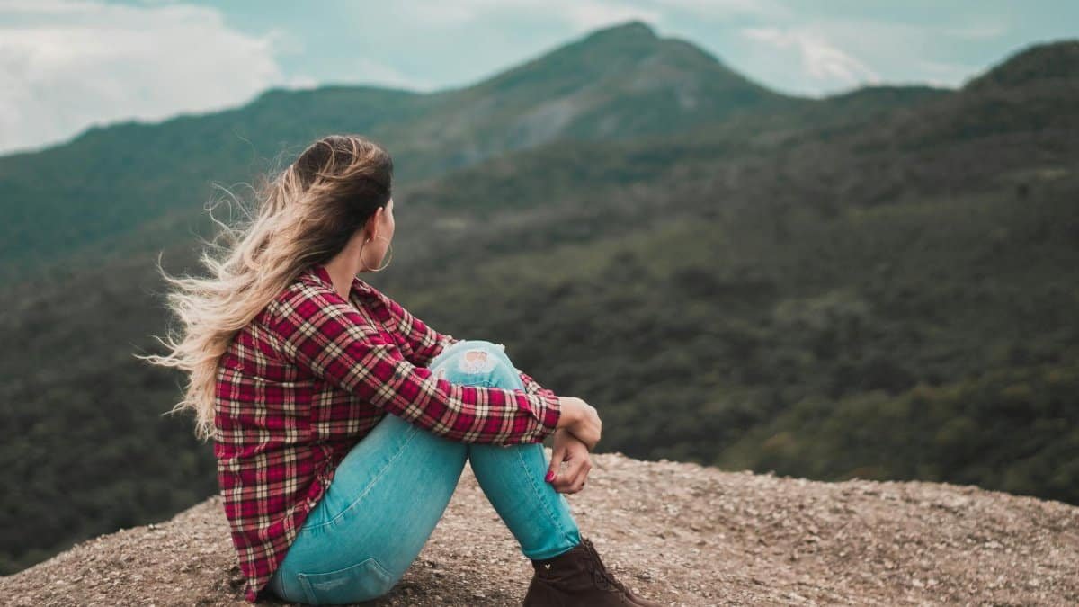 A woman in casual wear enjoys solitude on a scenic Brazilian mountain, embracing a moment of reflection.