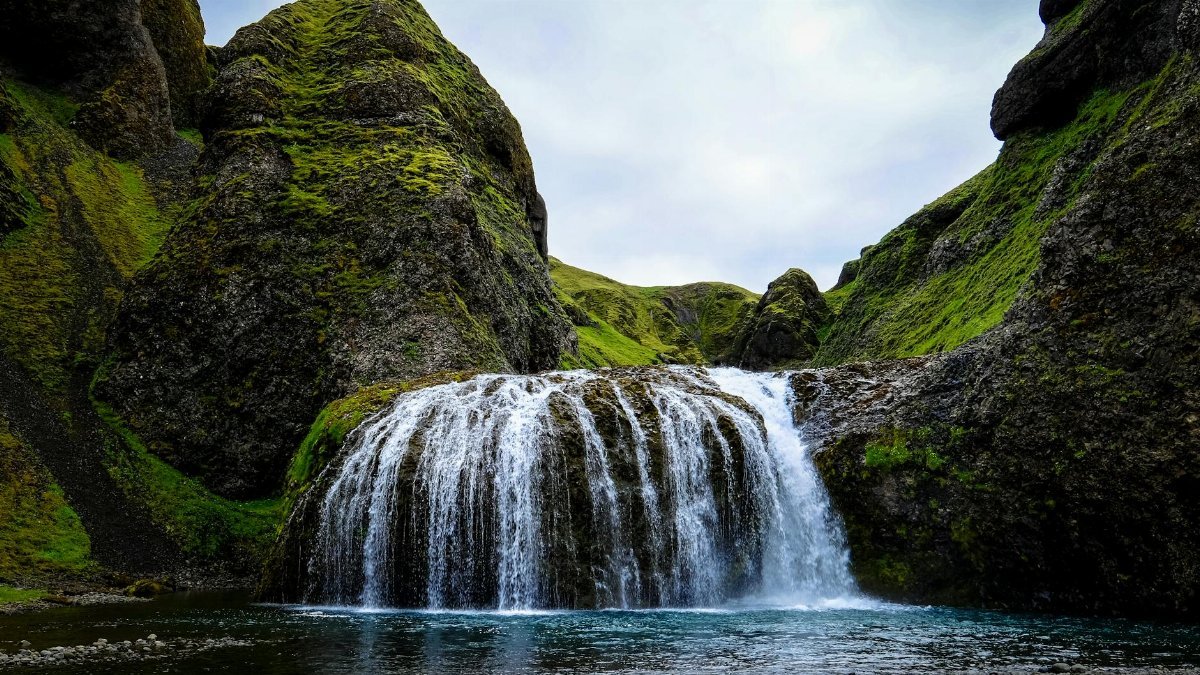 A beautiful waterfall cascading over moss-covered rocks in a mountain landscape, showcasing nature's serene beauty.