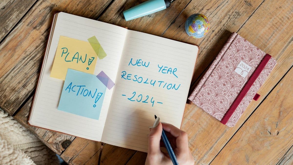 Person writing New Year resolution in a notebook with a pen, symbolizing goal setting for 2024.