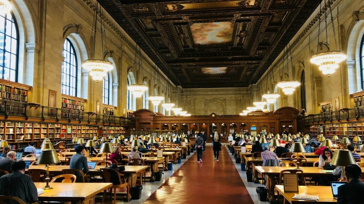 Busy reading room inside the New York Public Library featuring grand architecture.