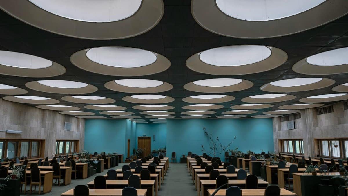 Wooden tables and chairs placed in rows in empty room of Vernadsky National Library of Ukraine with unusual round windows on ceiling
