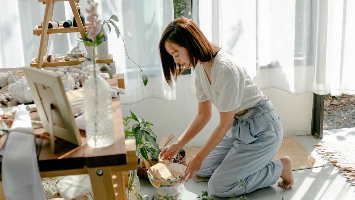 Side view full body of barefooted young ethnic female sitting on knees on floor while choosing tools for dyeing clothes with shibori technique