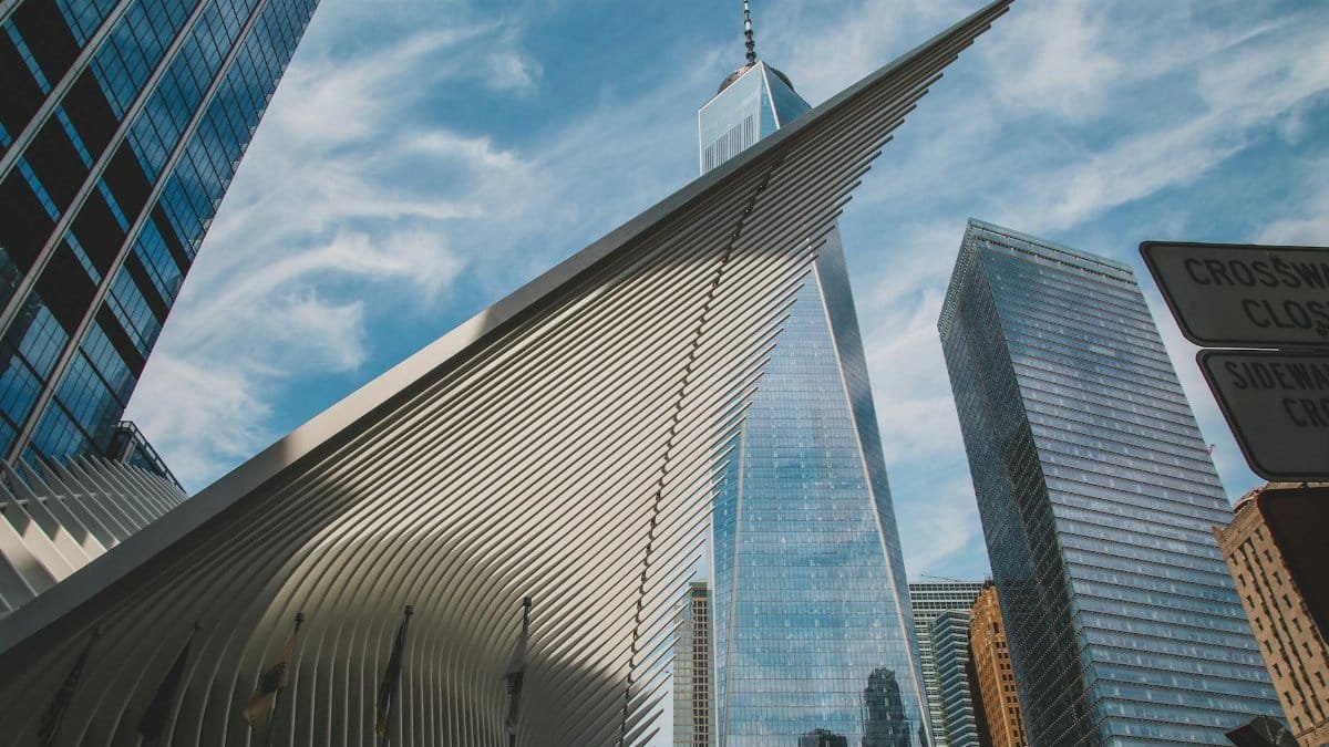 Dramatic angle of New York City's One World Trade Center and surrounding skyscrapers against a blue sky.