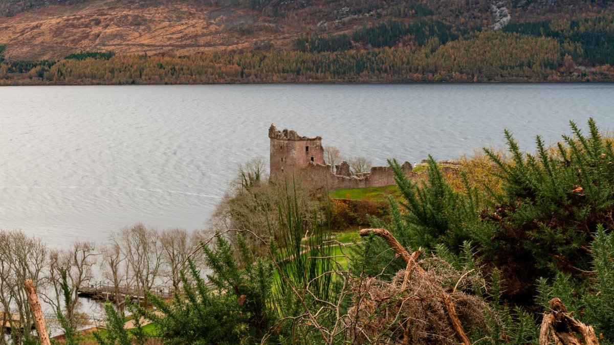 Breathtaking view of Urquhart Castle by Loch Ness surrounded by lush greenery and autumn colors.