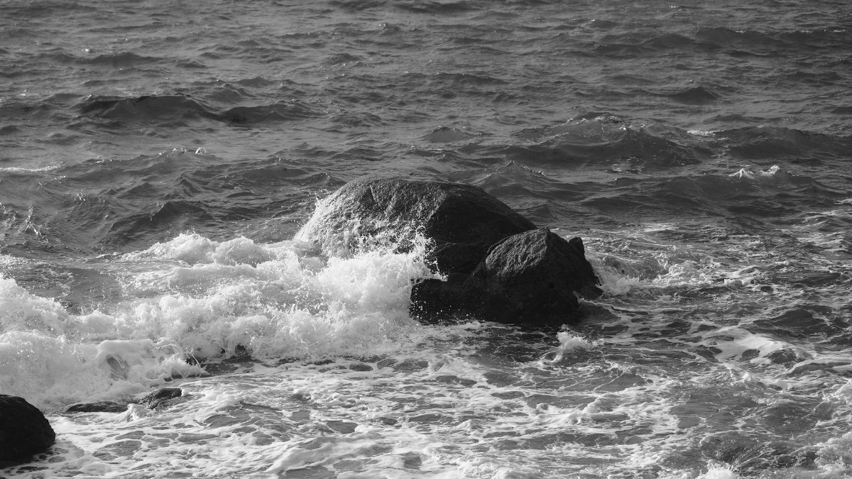 Dramatic seascape with waves crashing on rocks in grayscale, showcasing nature's power.