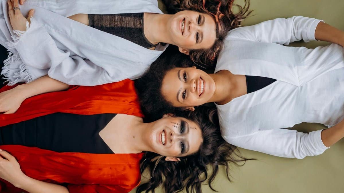 Three smiling women lying on the floor wearing vibrant clothing, symbolizing joy and friendship.
