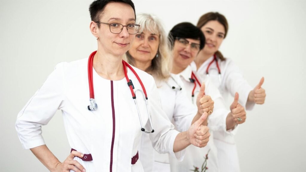 A group of female doctors in white coats showing thumbs up, symbolizing teamwork and women empowerment in healthcare.