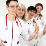 A group of female doctors in white coats showing thumbs up, symbolizing teamwork and women empowerment in healthcare.