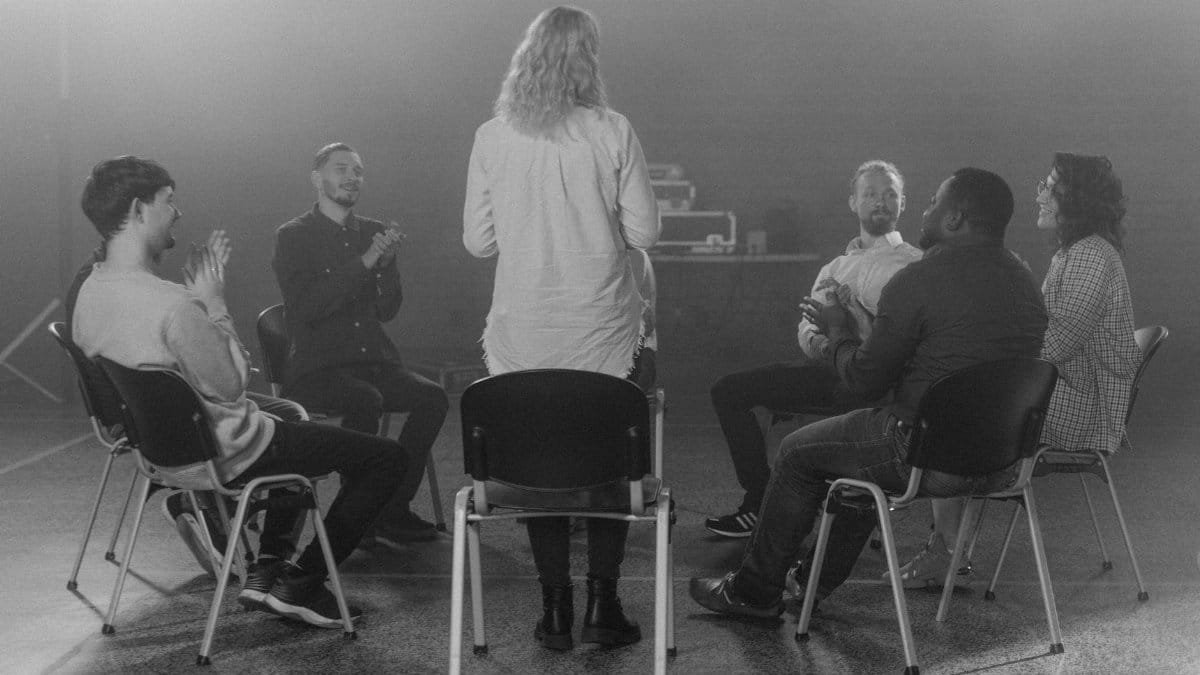 Black and white photo of a diverse group therapy session, fostering open discussion and support.