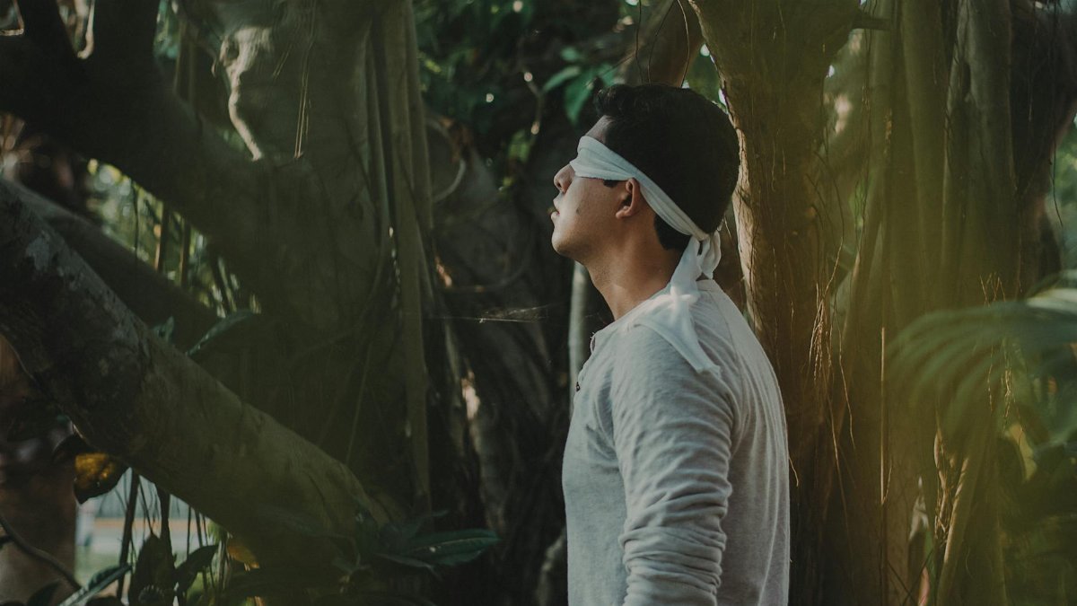 A man stands blindfolded in a serene forest, exploring nature.
