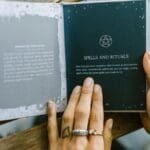 Close-up of hands holding an open book about spells and rituals, featuring a pentagram symbol.