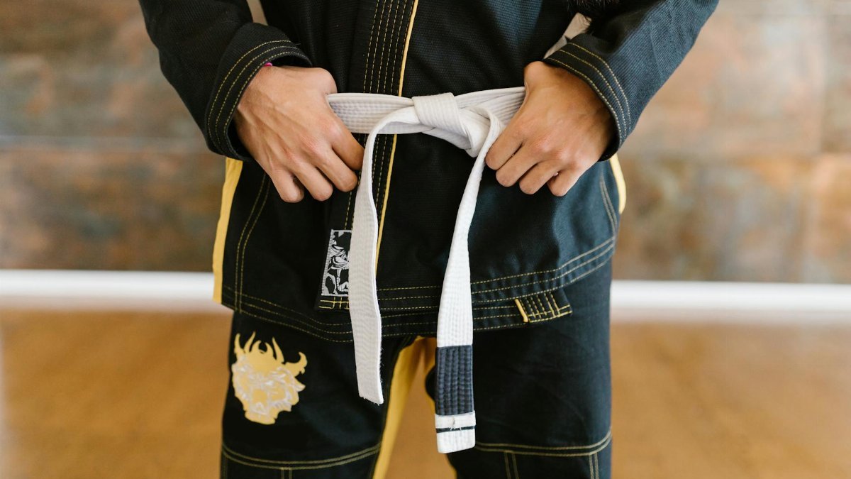 Martial artist preparing for practice by tying a white belt in traditional uniform.