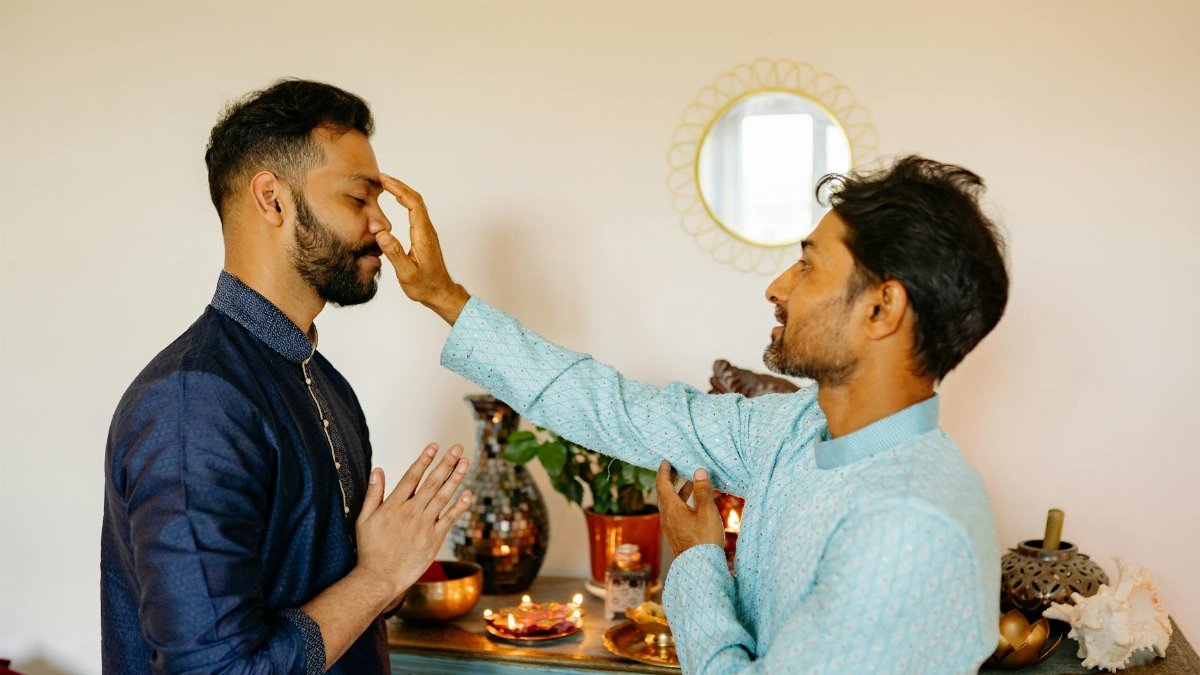 Two Indian men engaged in a forehead marking ritual during a traditional Hindu ceremony.