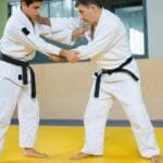 Two men engaged in a judo training session on a mat indoors. Strength and technique in action.