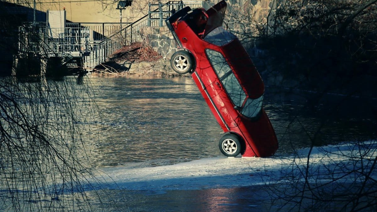 A striking image of a red car tipped into a frozen river in Sweden during winter.