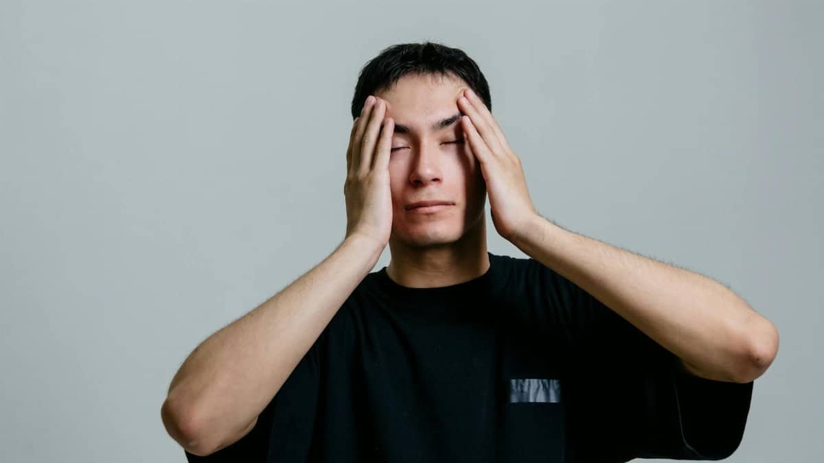 Man experiencing stress, hands on head, isolated on a gray background.