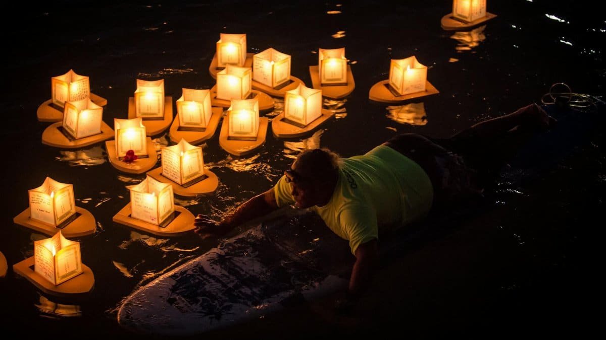 A person observes floating lanterns illuminating the night waters in Honolulu, Hawaii.