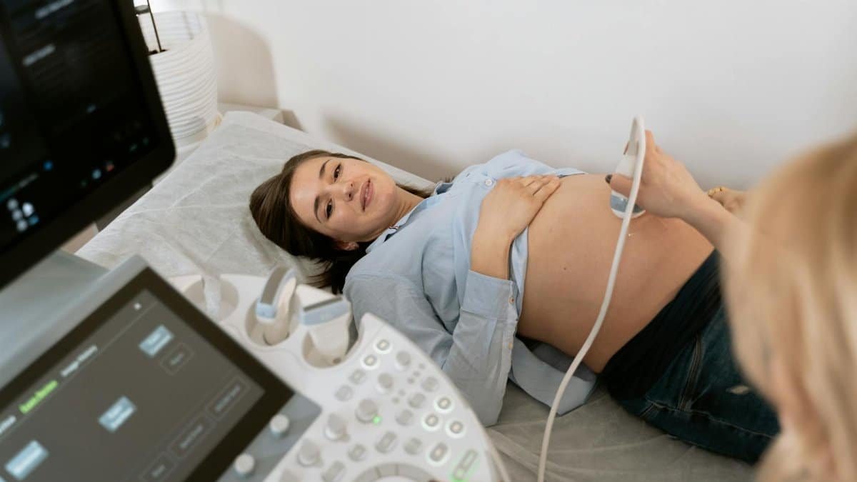 Pregnant woman undergoing an ultrasound scan, assisted by a healthcare professional in a medical clinic.