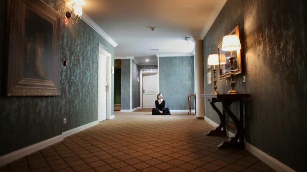 A woman sits peacefully in a luxurious hallway with elegant lamps and decor.