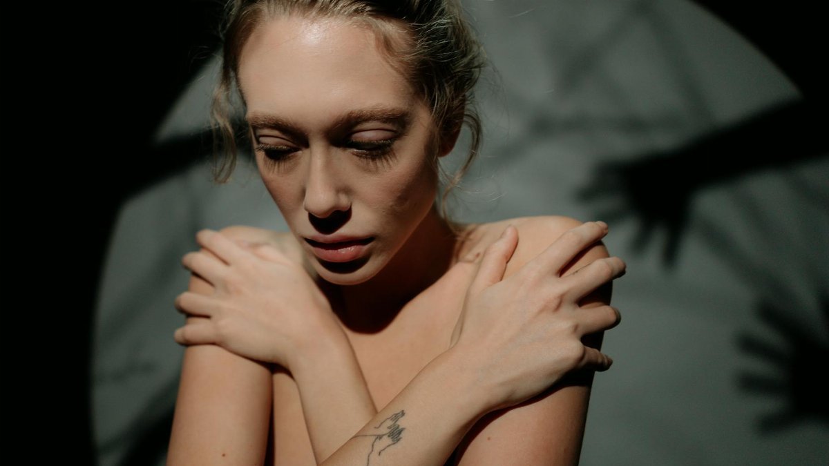A woman hugging herself in a shadowy setting, conveying fear and introspection.