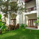 Elegant villa exterior with lush lawn and tropical plants in a summer setting.